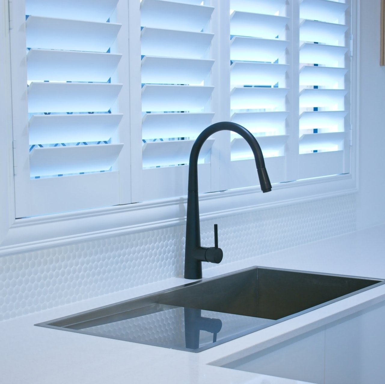 Close up of stylish black tapware over kitchen sink, framed by slightly open plantation shutters.