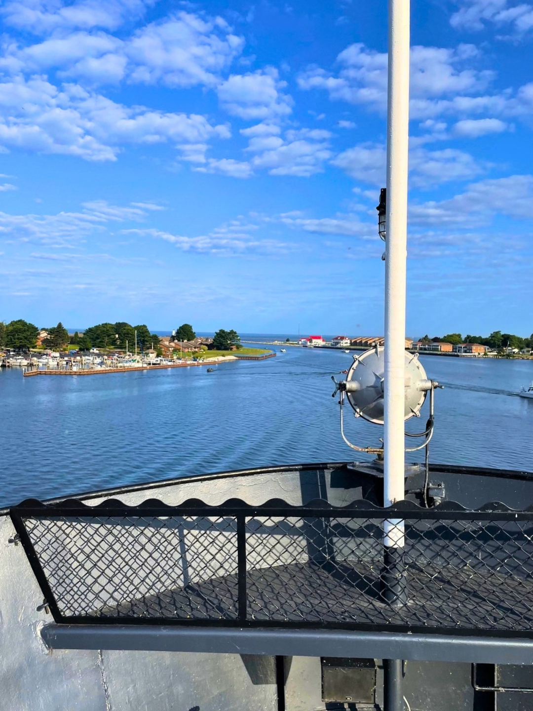 View from a ferry deck across a calm river toward a shoreline under a blue sky