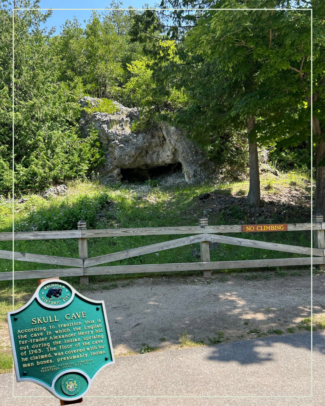 Rocky cave entrance behind a wooden fence and green historical marker in a leafy park