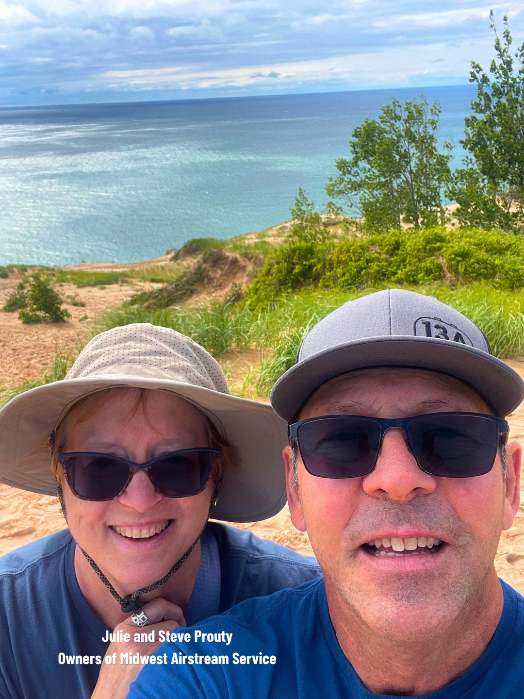 Two smiling people in hats and sunglasses taking a selfie on a seaside cliff with ocean behind them
