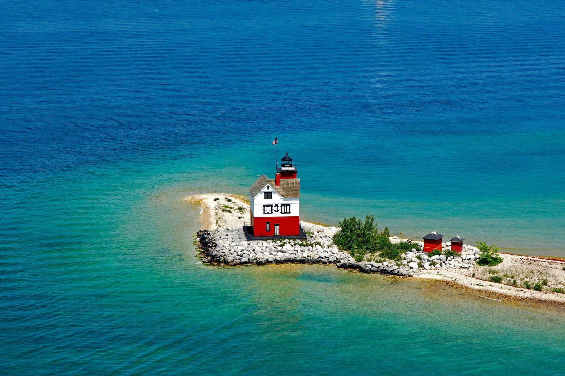 Red and white lighthouse on a rocky island in turquoise-blue sea under clear sky