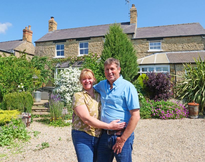 Couple smiling in front of a stone farmhouse in France