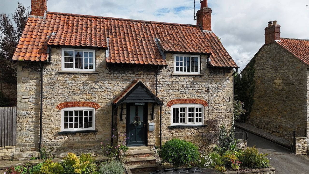Stone cottage with red-tiled roof and white-trimmed windows. A small porch covers the dark front door.