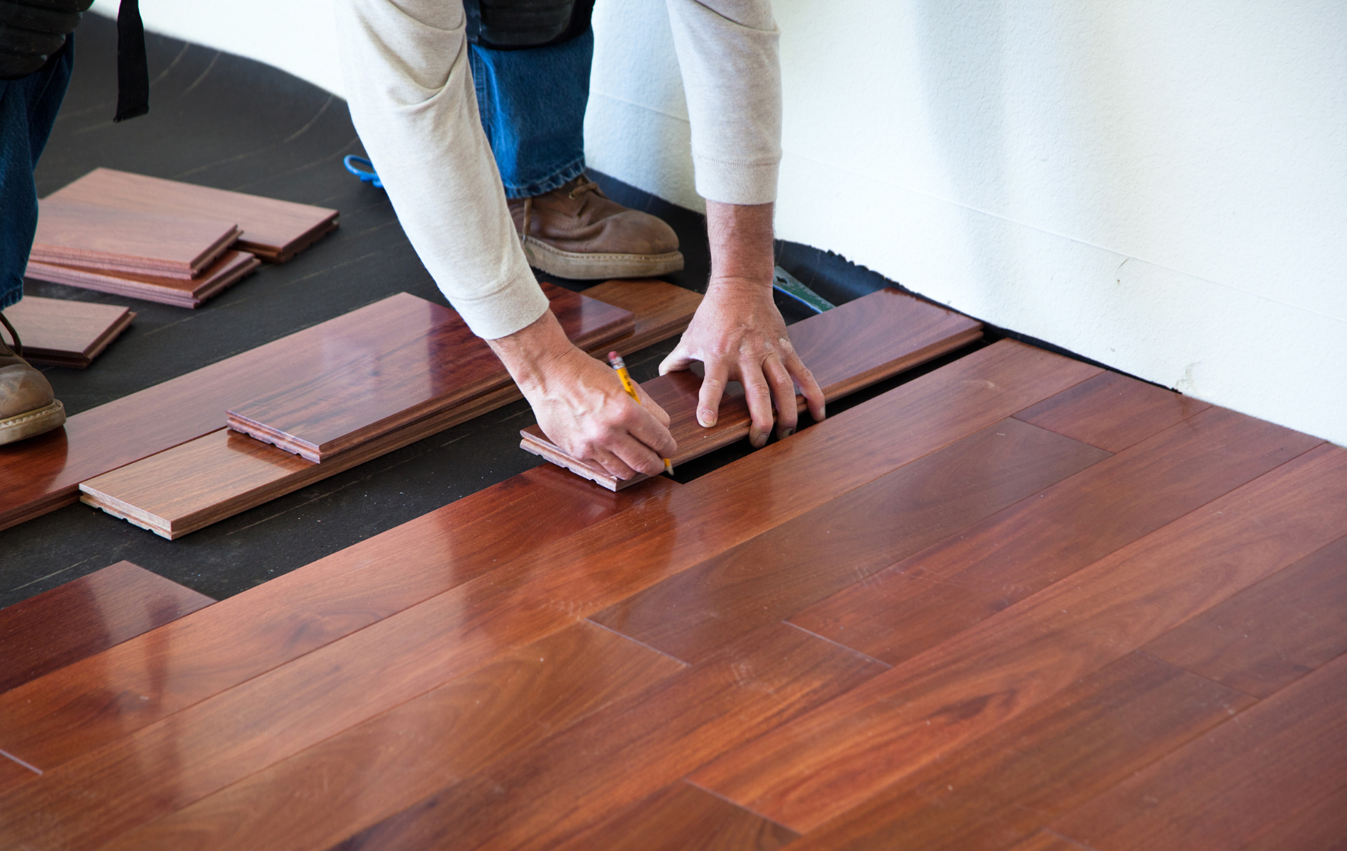 A man is installing hardwood flooring in a room.