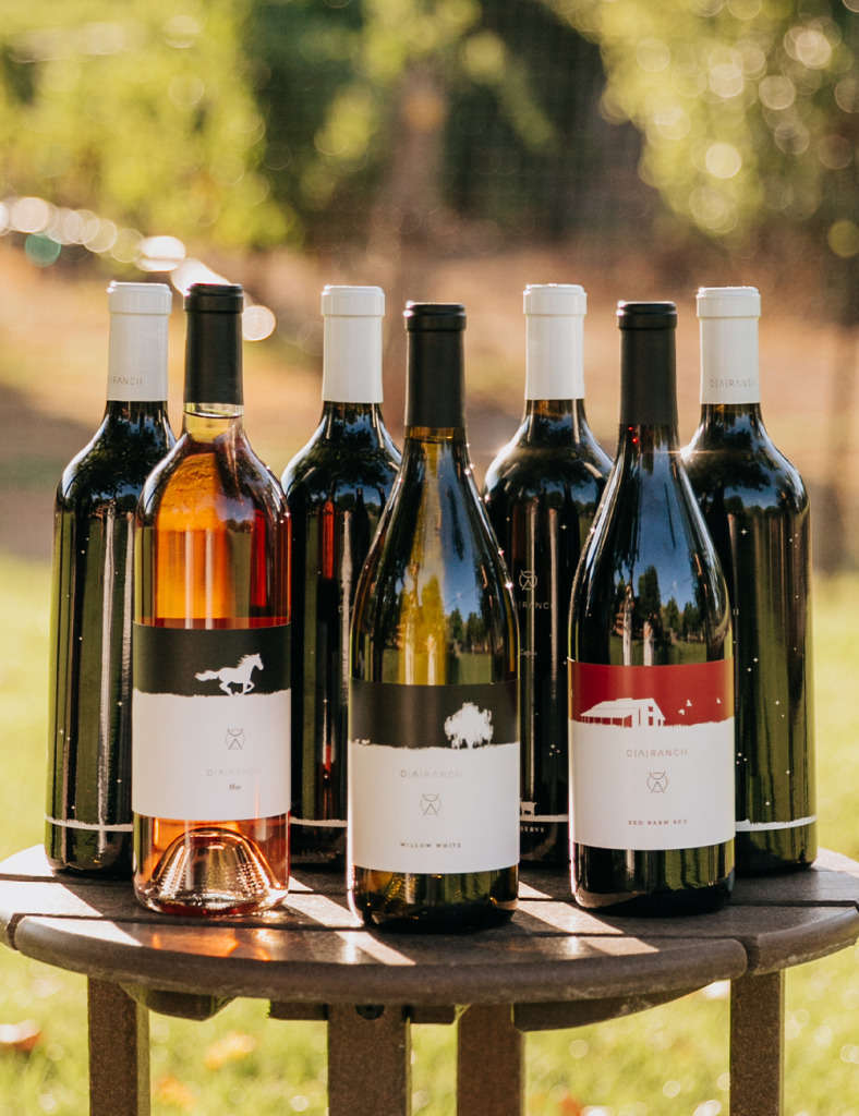 Collection of wine bottles on a wooden table outdoors with a blurry green background.
