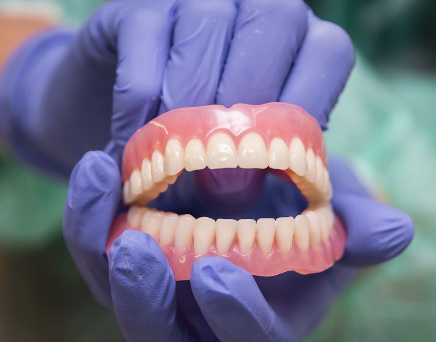 Gloved Hands Holding a Full Set of Upper and Lower Dentures in a Dental Clinic — Smiles On Hobart in Glenorchy, TAS
