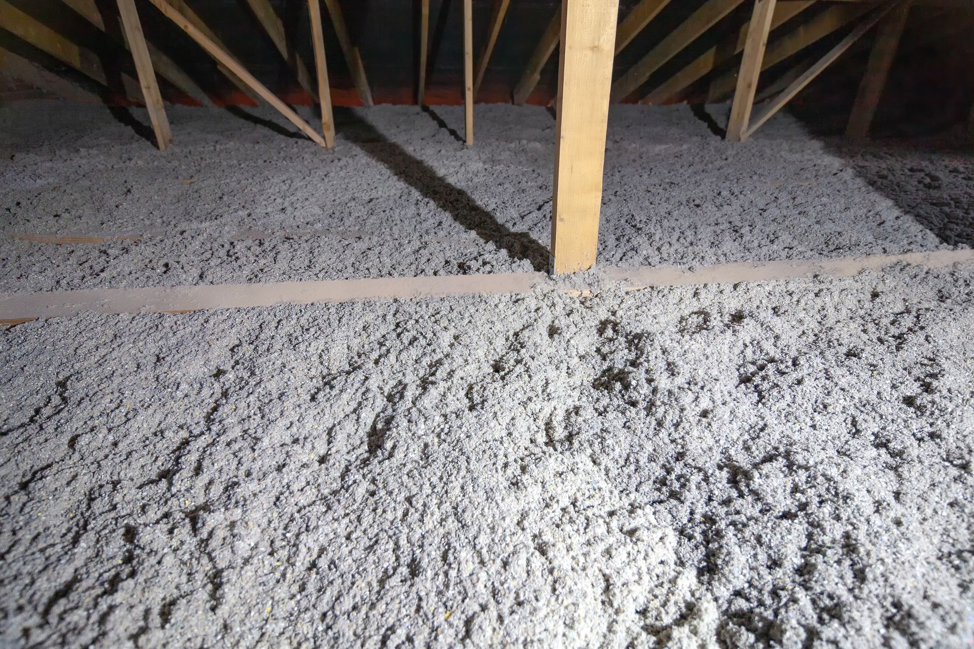 A man is working on a pipe in an attic.