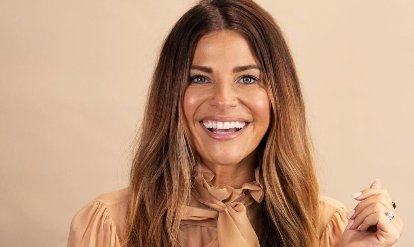 Smiling woman with long brown hair in a beige blouse against a soft beige background