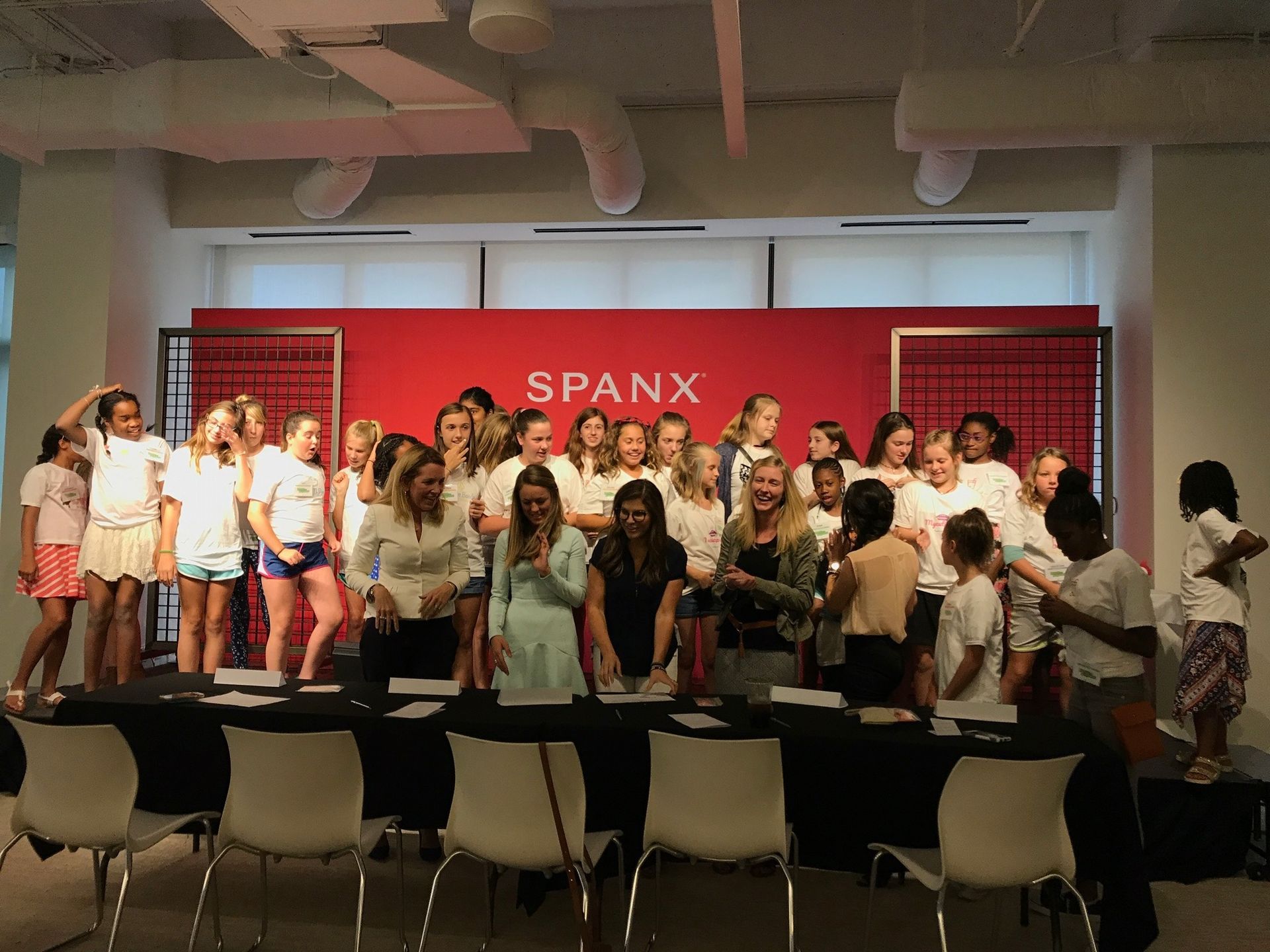 Group of models on a runway stage in front of a red SPANX backdrop, posing for an event.