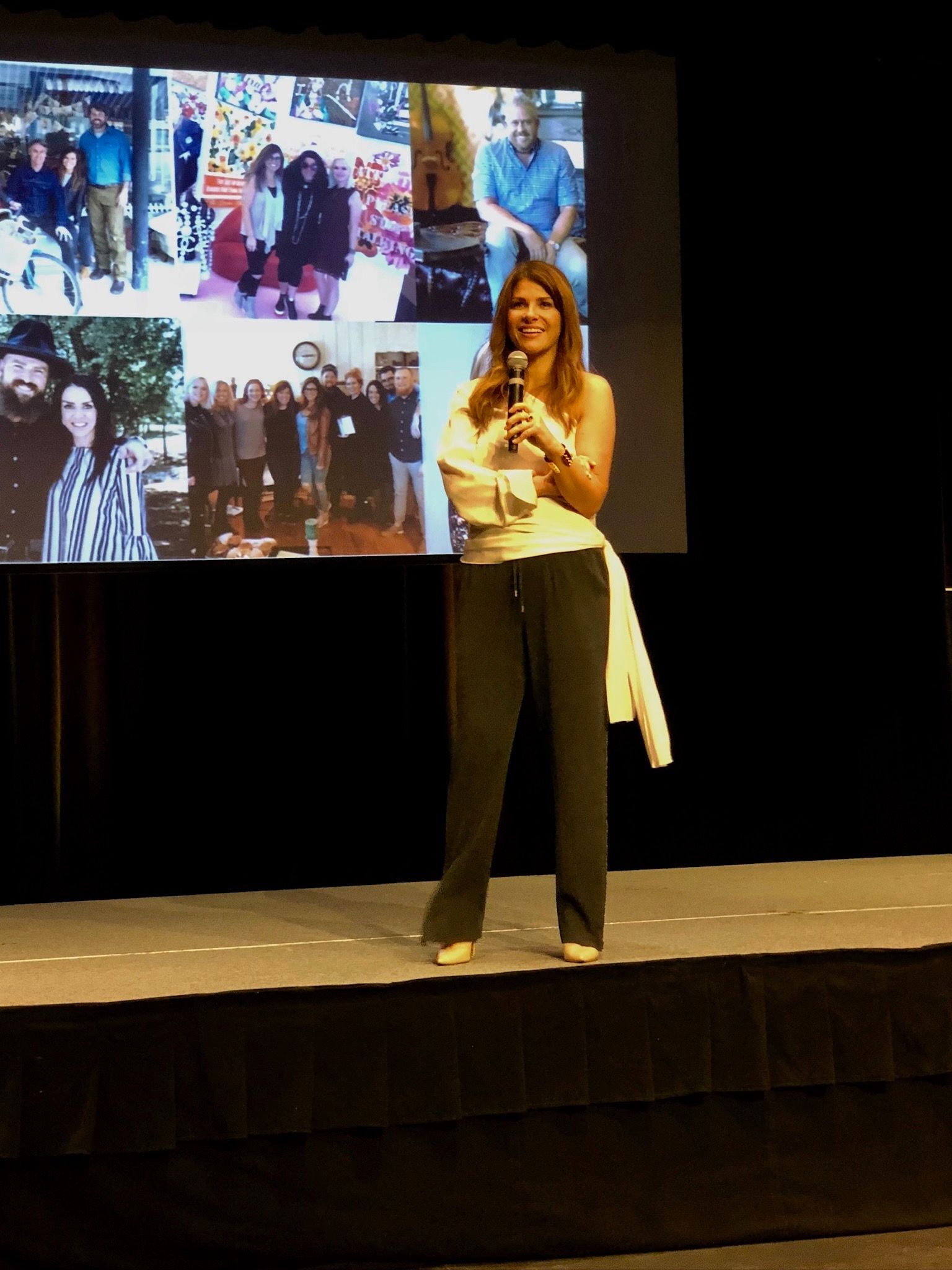 Presenter speaking on a stage in front of a large photo collage backdrop.