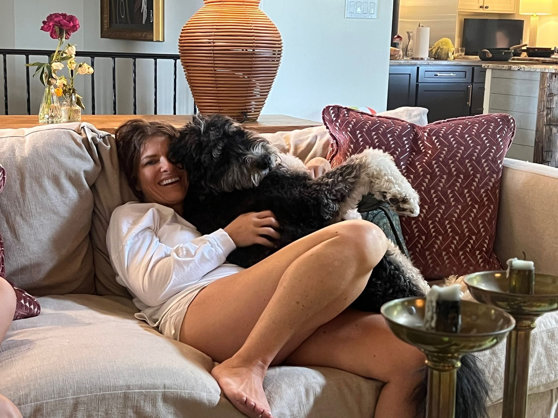 Woman cuddling a fluffy black dog on a beige couch in a cozy living room