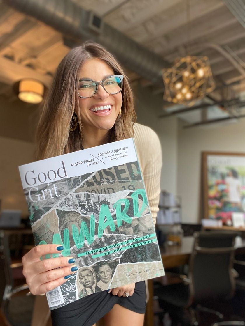 Woman smiling and holding a magazine in a café, with warm lights and modern decor in the background