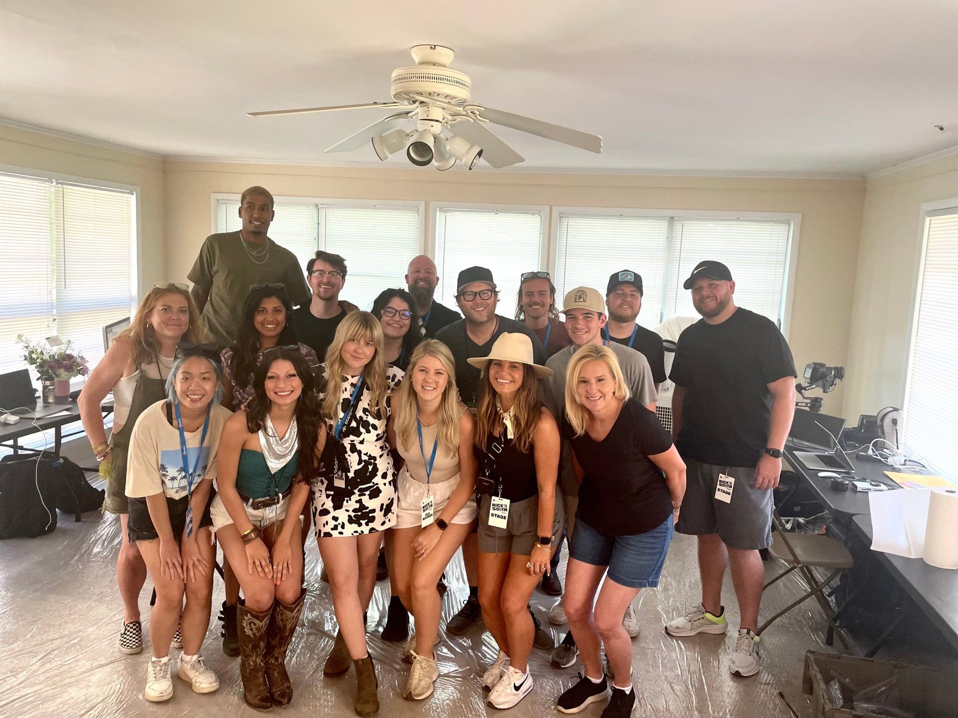 Group of people posing together in a bright living room with white windows and a ceiling fan.