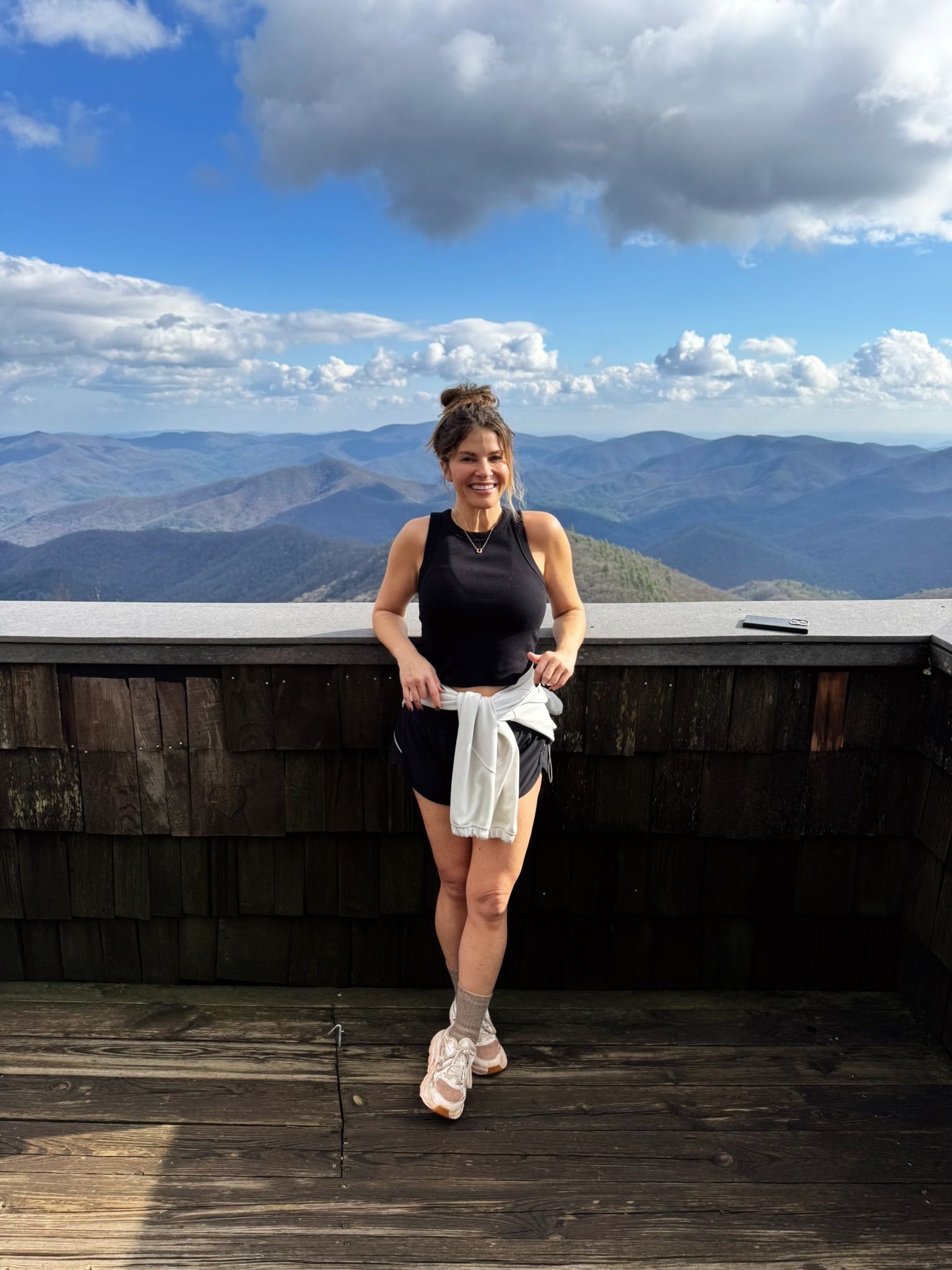 Person standing on a mountain overlook with cloudy sky and distant blue ridges behind them