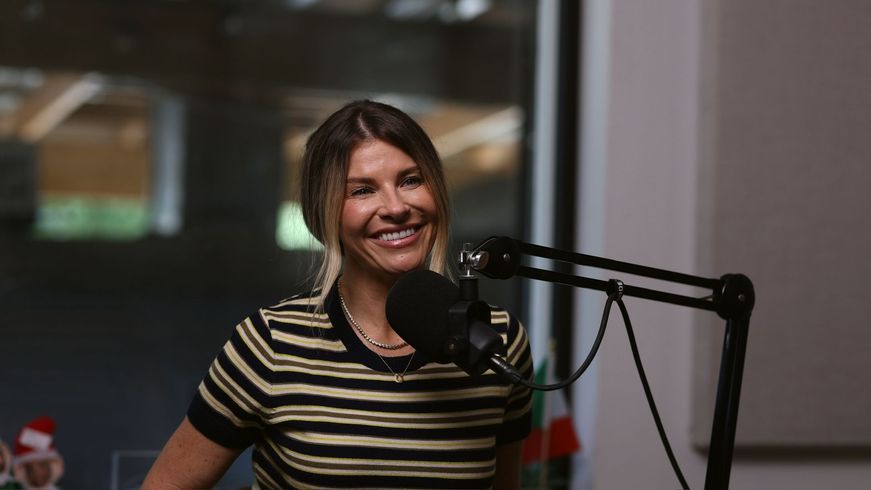 Smiling woman speaking into a microphone in a podcast studio, wearing a striped shirt