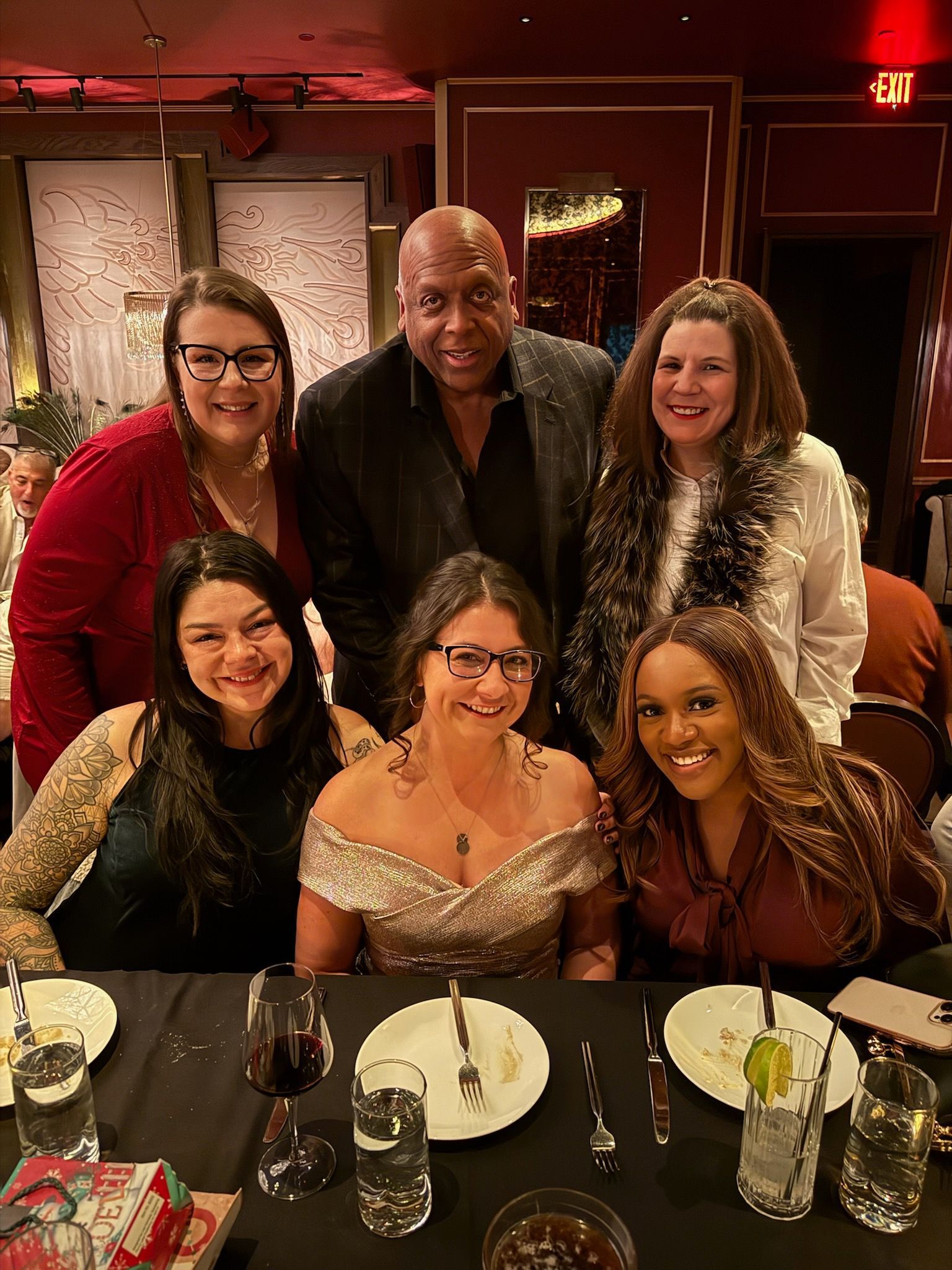 Group of people at a formal dinner, smiling at the camera. Dark setting with red accents.
