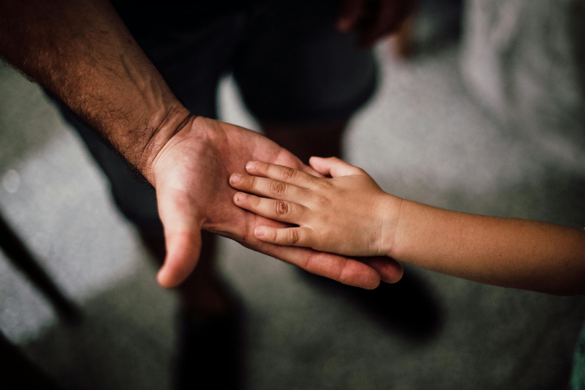 Adult's hand holding a child's hand, touching. Skin tones vary.