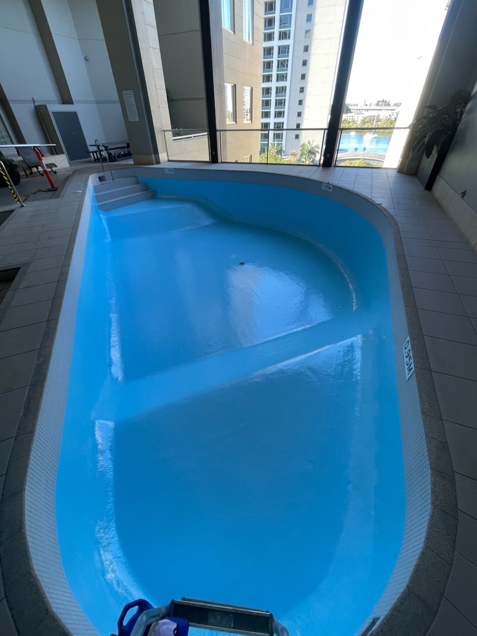 Empty blue swimming pool on a rooftop terrace with gray tile decking and city views