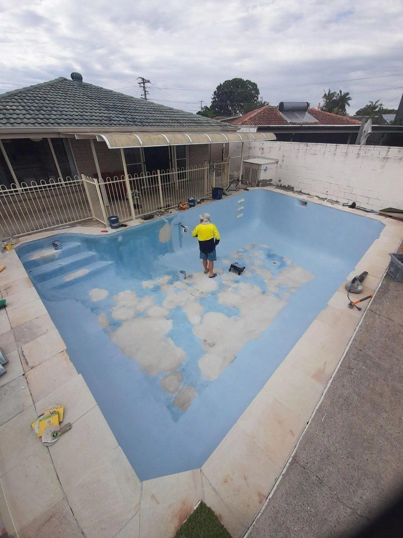 Person in a yellow shirt working in an empty blue swimming pool under renovation.