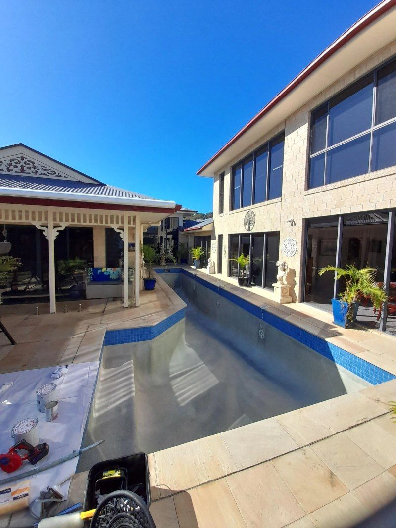 Sunny courtyard with empty blue-tiled pool between a gazebo and a beige building.