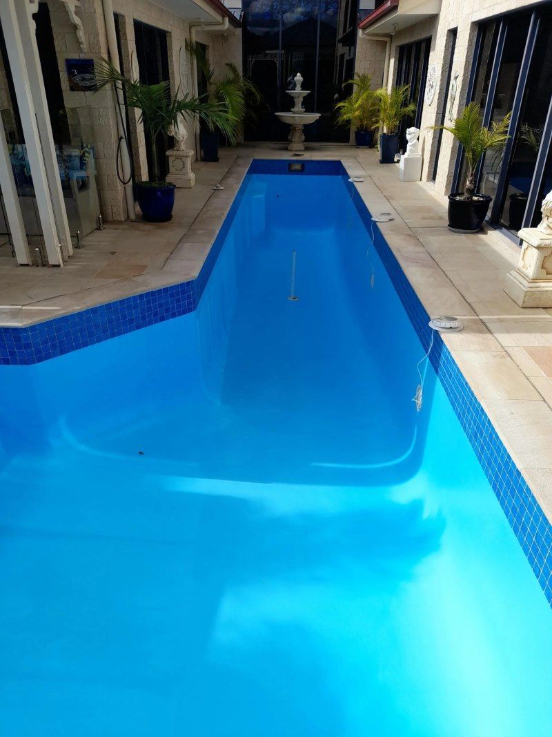 Long blue swimming pool in a courtyard with white tile and a fountain at the far end