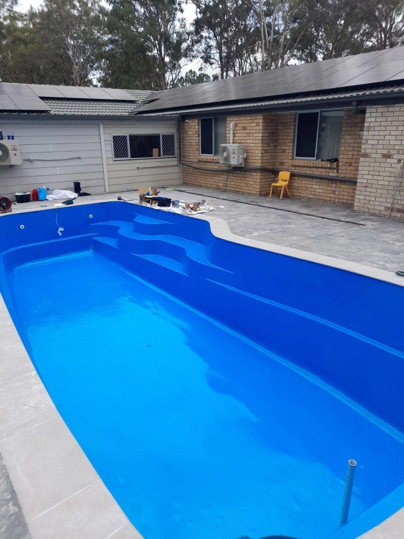 Backyard swimming pool with bright blue liner beside a brick house and patio.