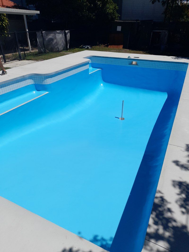 Empty blue swimming pool in a sunny backyard, with steps and a pool vacuum hose.