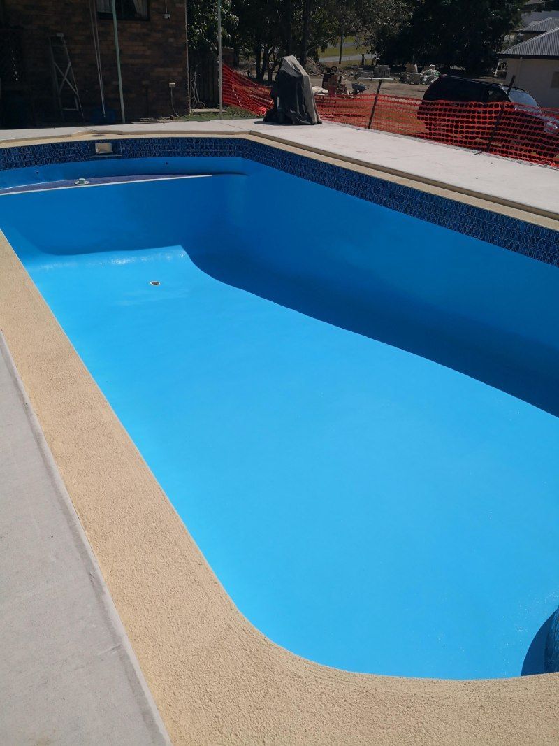 Empty blue swimming pool with tan coping and red safety fencing in the background