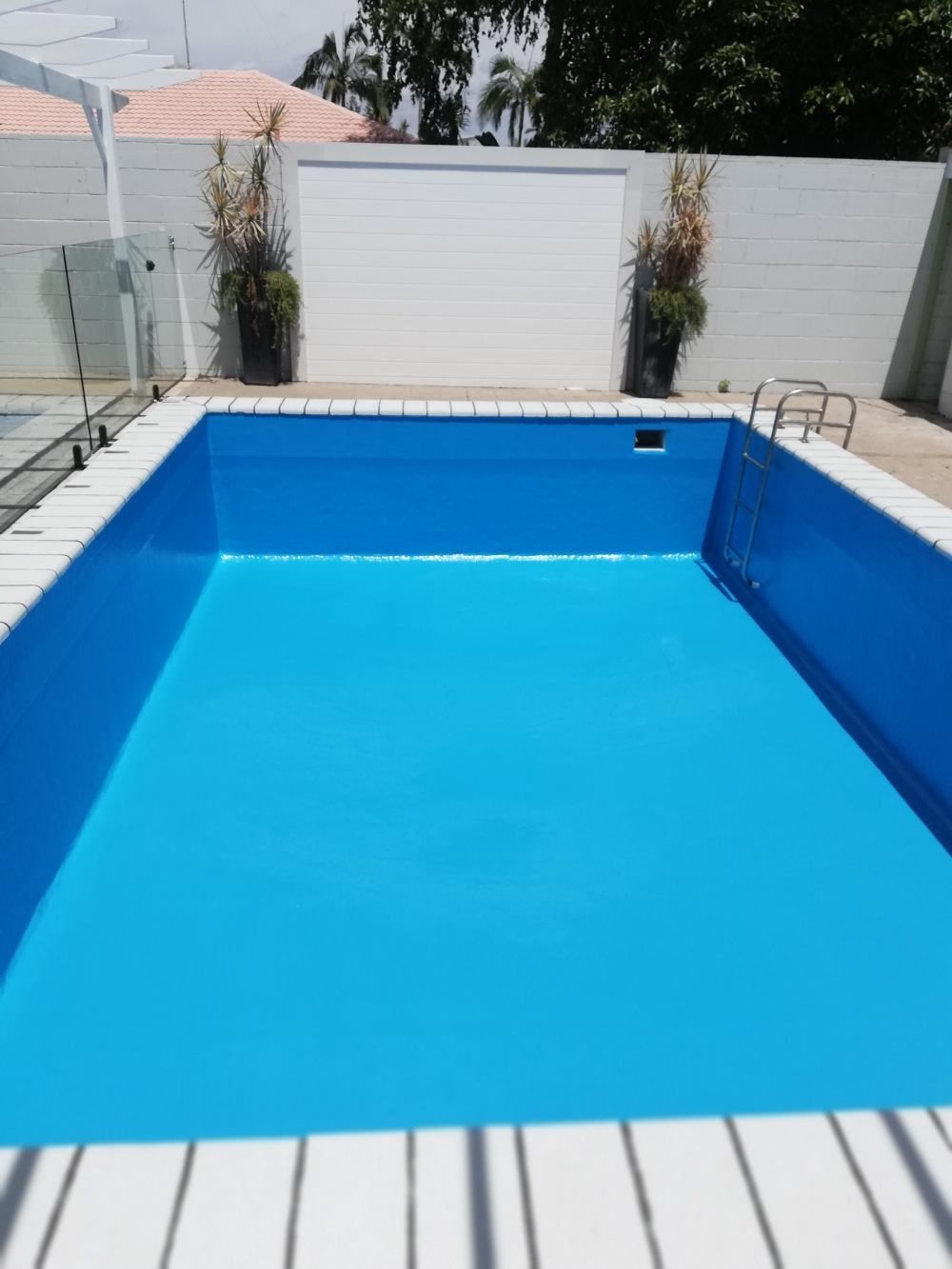 Bright blue empty swimming pool with white deck and fence, viewed from the shallow end