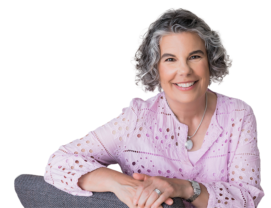 A woman in a pink shirt is sitting on the floor with her hands folded and smiling.