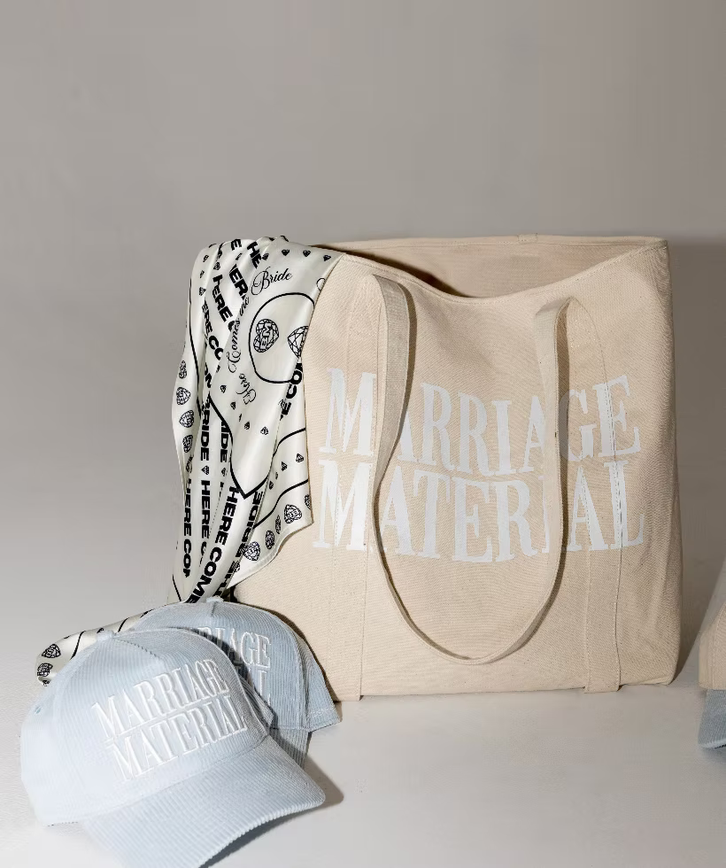 Beige tote bag with white text, black-and-white scarf, and light blue cap on a shelf