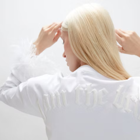 Person with long blonde hair adjusting it against a bright white background