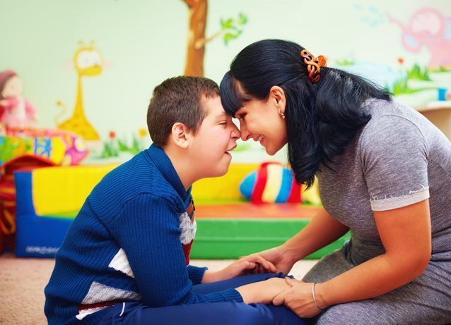 A child and an adult sitting on the floor in a room, leaning toward each other with their foreheads touching.