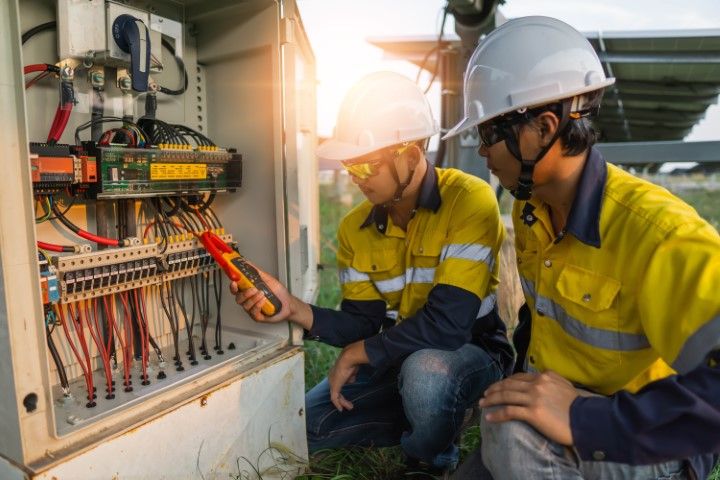 Electrician inspecting an open circuit breaker panel with tools at an outdoor utility box.