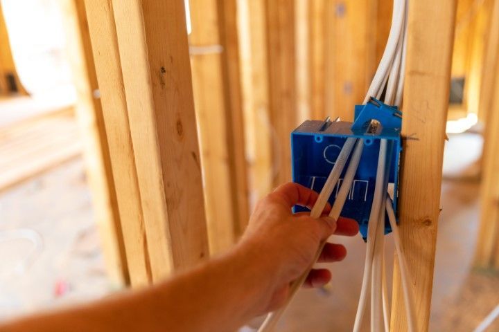Electrician in a hard hat testing wiring inside an open electrical panel