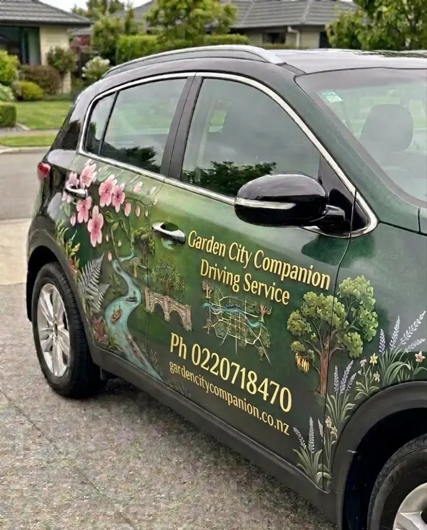 Green car with garden company signage parked on a suburban street