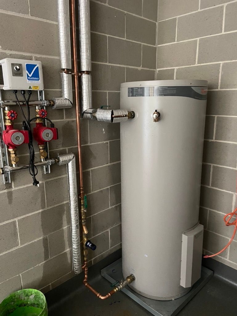 Water heater and related piping against a brick wall. Includes pumps, valves, and a control unit. — All Stars Plumbing In Dapto, NSW