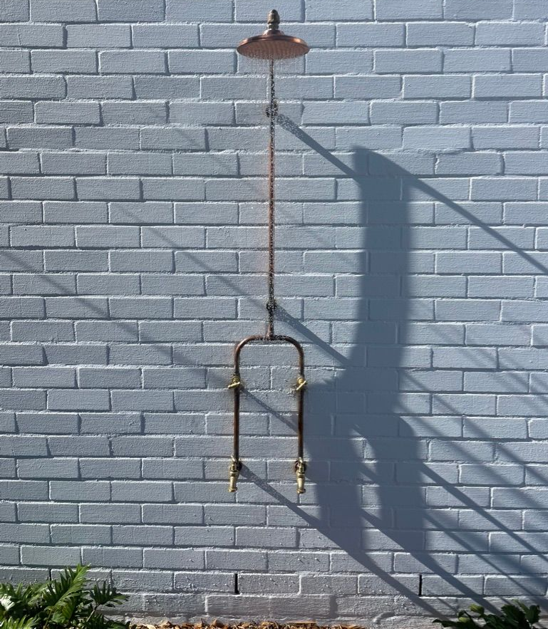Outdoor shower fixture against a painted brick wall; copper colour with rain shower head. — All Stars Plumbing In Dapto, NSW