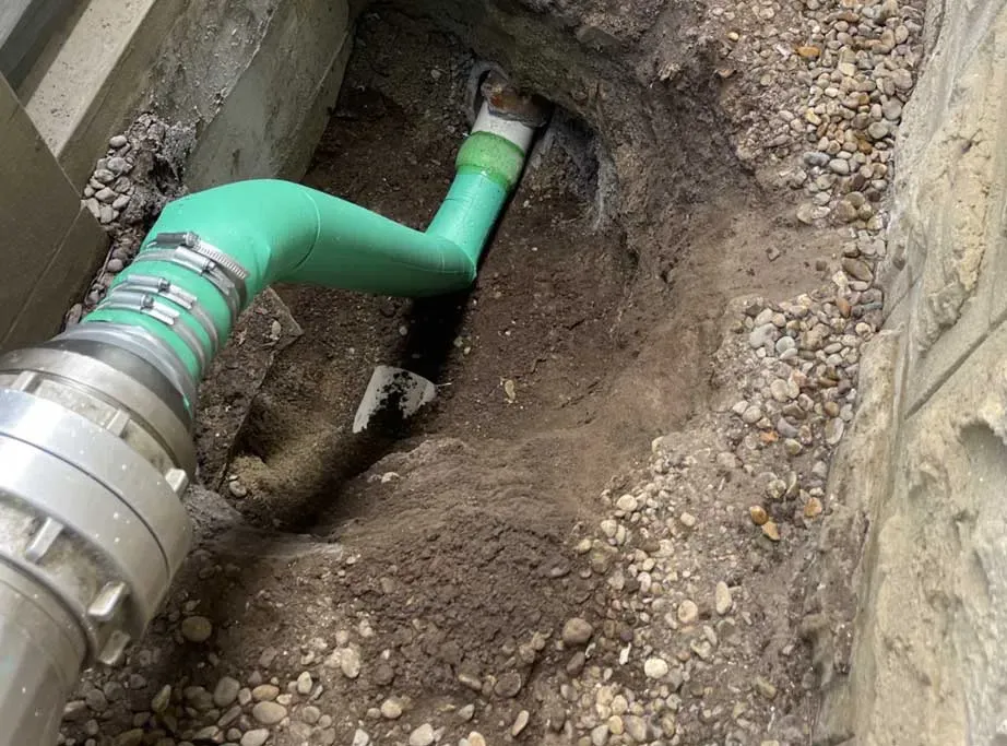 Green plumbing pipe in dirt trench next to concrete foundation, connected to a metal pipe. — All Stars Plumbing In Dapto, NSW