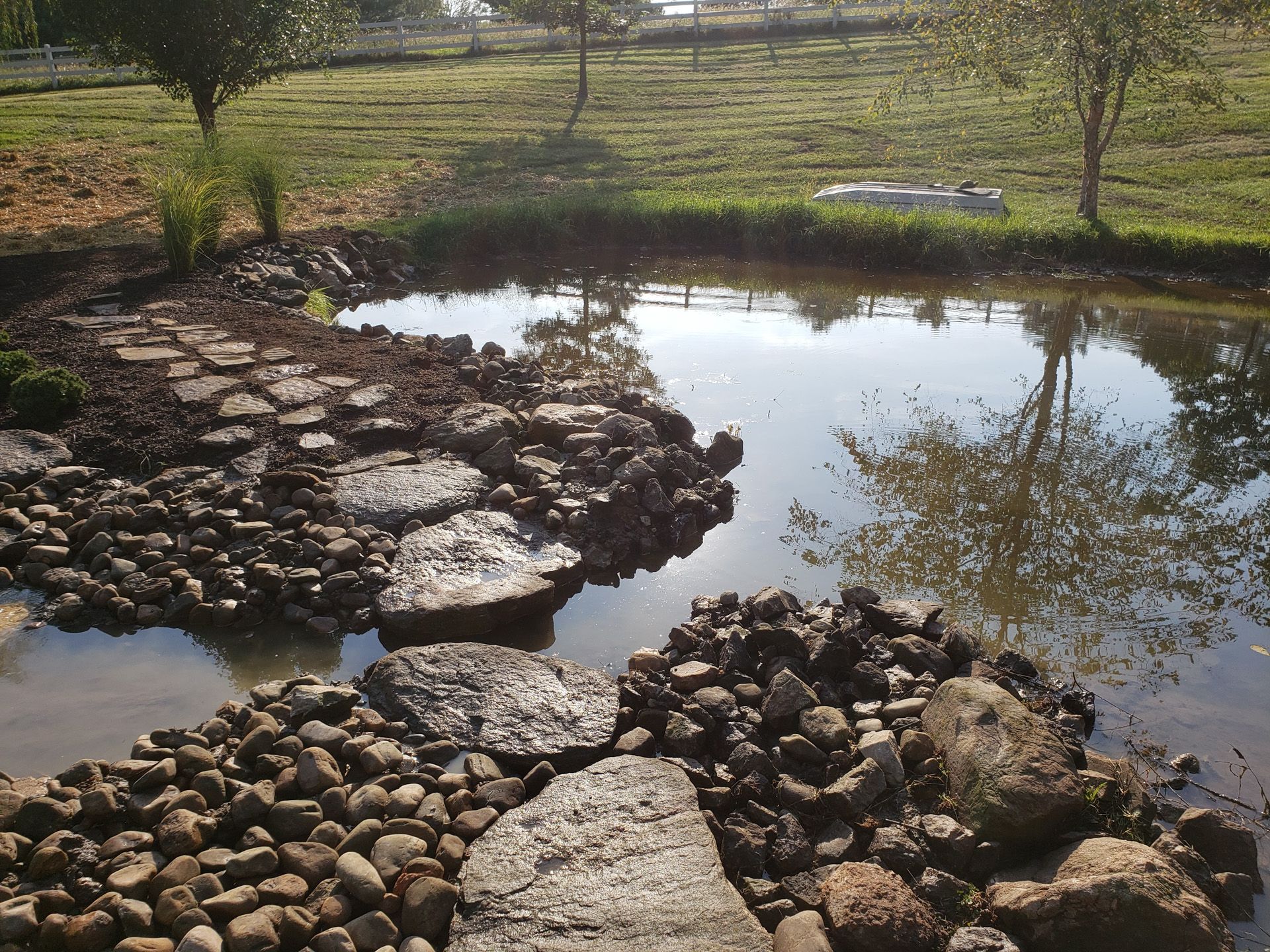 A pond surrounded by rocks and grass with trees in the background