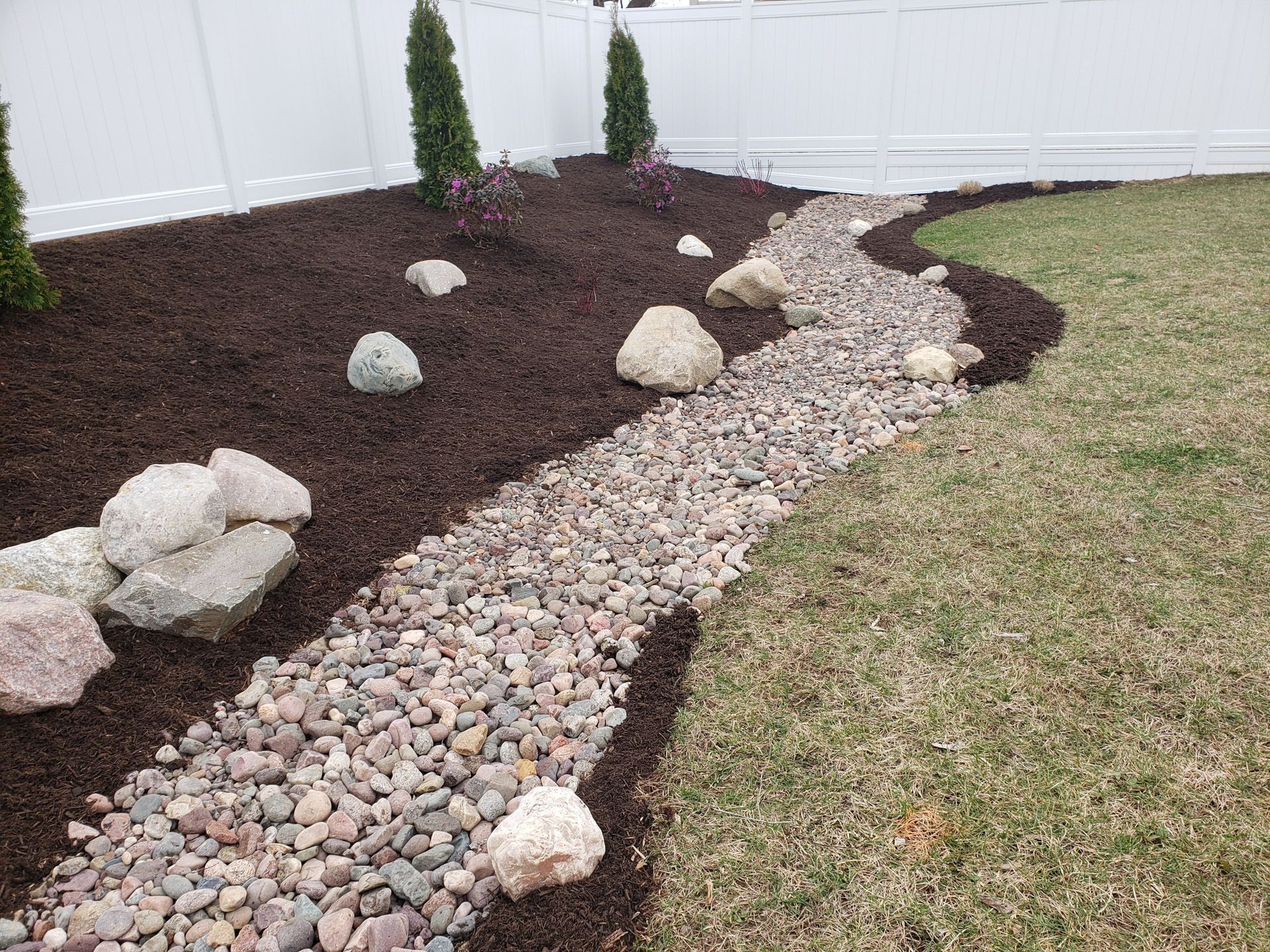 A rocky path leading to a white fence in a backyard.
