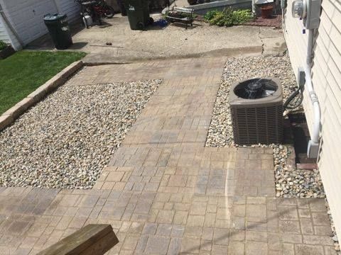 A brick walkway leading to a house with a air conditioner.