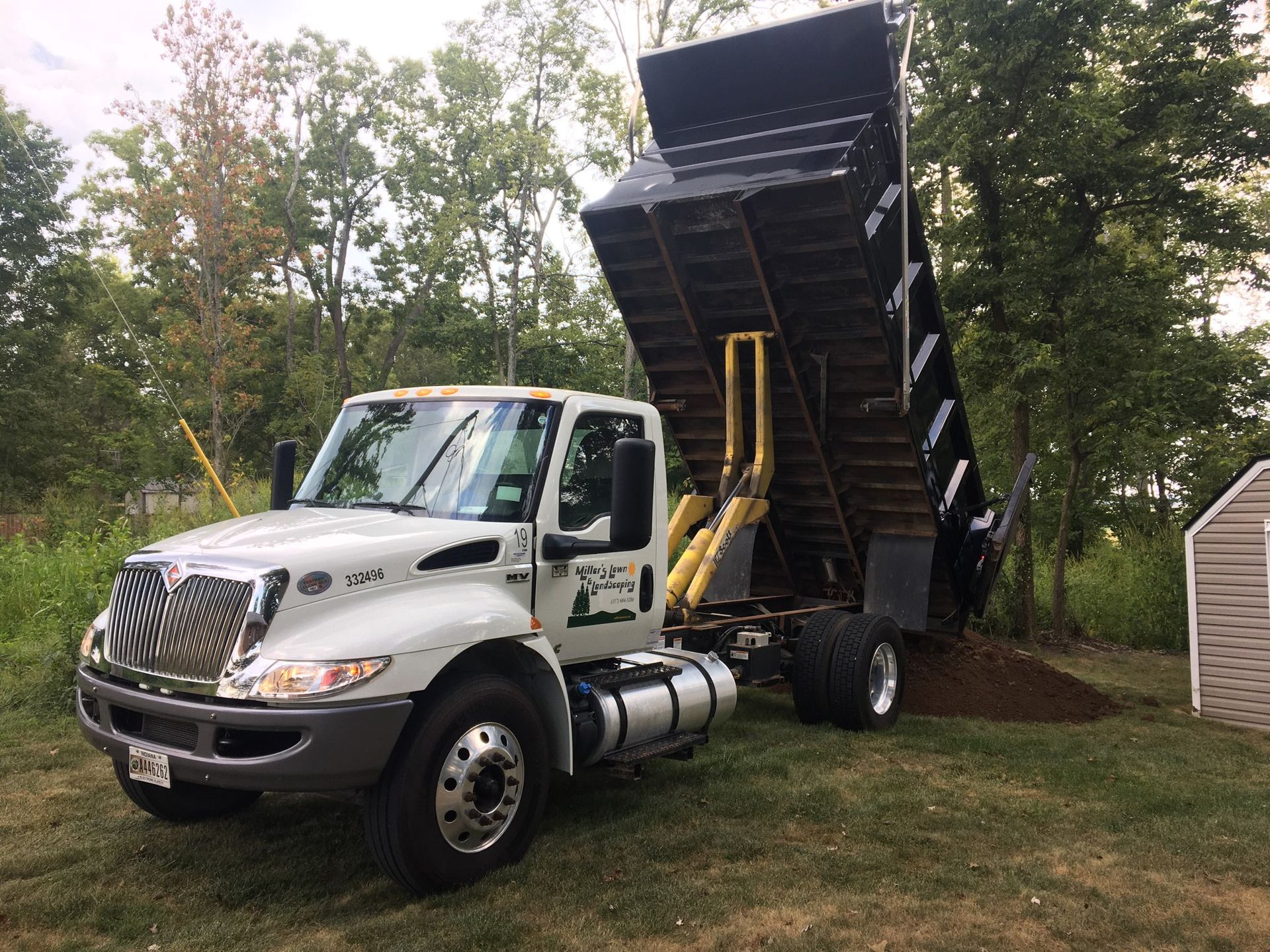A dump truck is parked in a grassy field next to a shed.