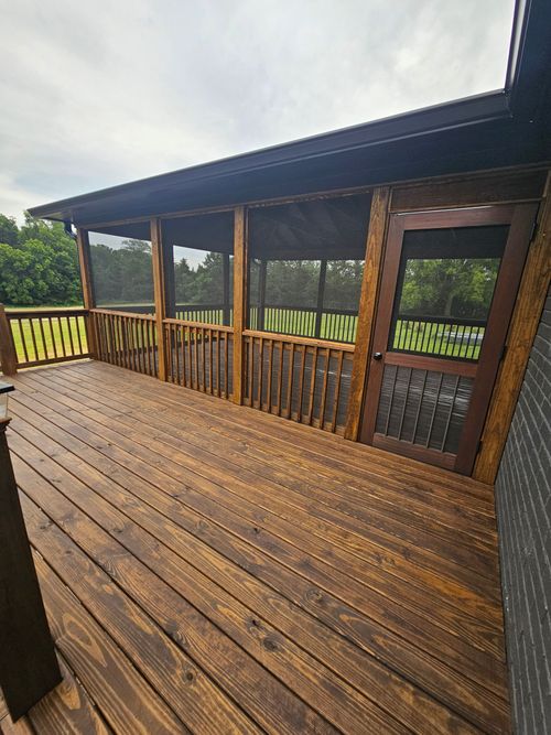 Wet wooden deck with covered porch and railing overlooking a green landscape under cloudy skies