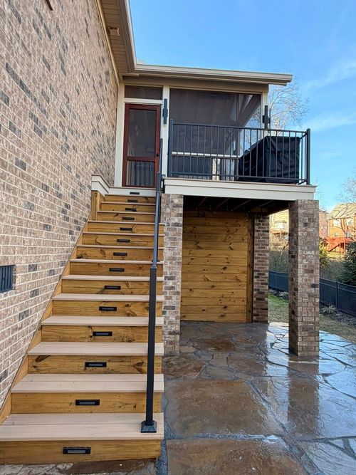 Outdoor metal staircase beside brick house leading to a small upper deck with railing and covered patio below