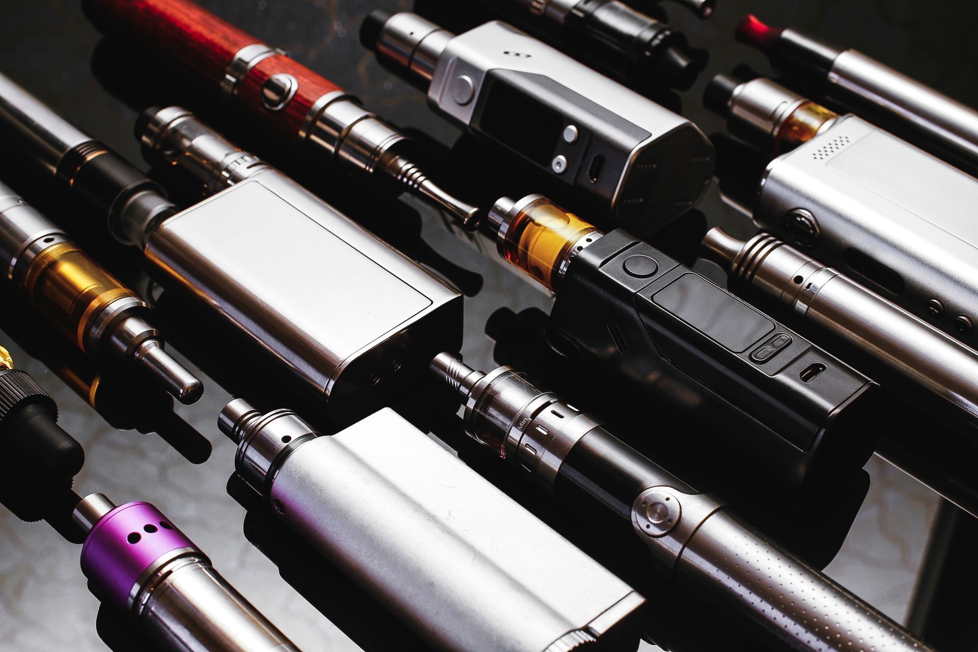 Assorted colorful vape pens arranged in rows on a dark display surface