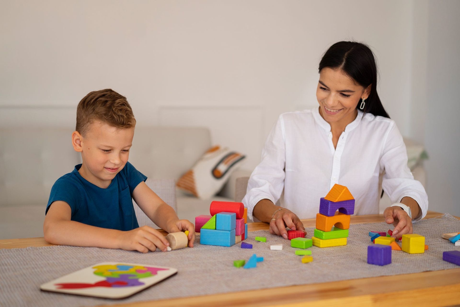 A woman and a child playing with colorful building blocks at a table. They are smiling.
