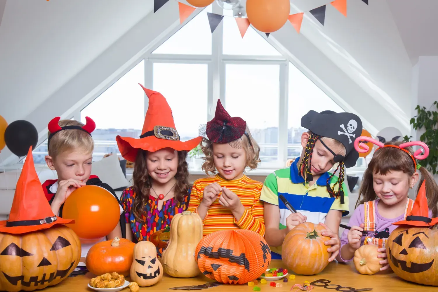 Children in Halloween costumes carving pumpkins at a table with decorations.