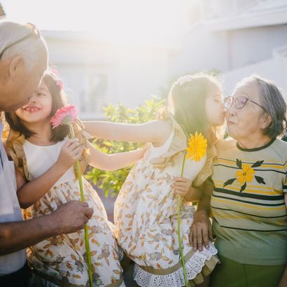 A little girl is kissing an older girl on the cheek while holding flowers.