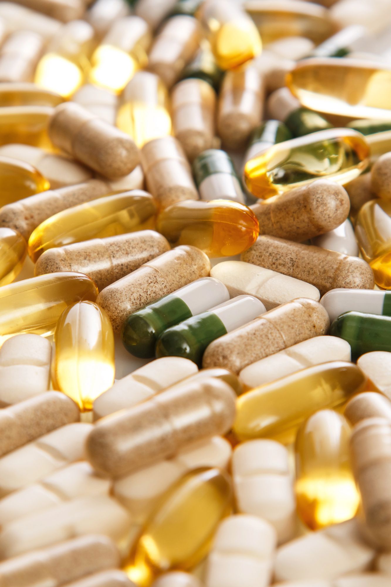 Surtido de cápsulas y cápsulas blandas de vitaminas y suplementos en colores blanco, dorado, verde y ámbar.